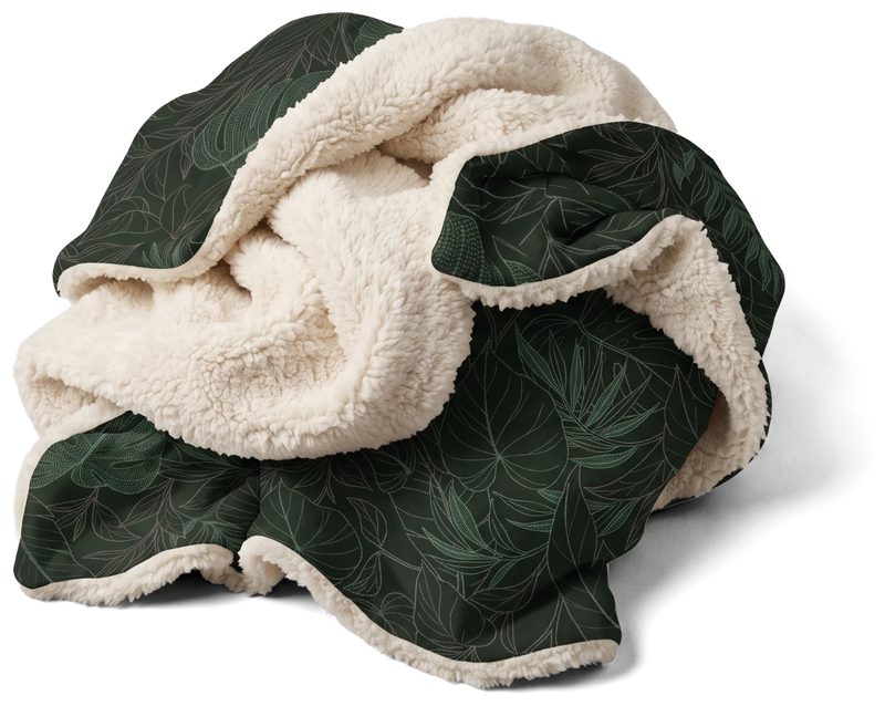 Jungle blanket crumpled into a loose heap, the dark green printed face folding around the plush ivory sherpa reverse